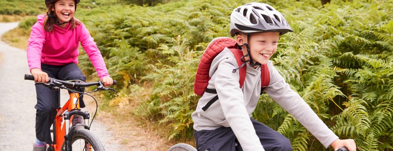 Two young children smiling as they cycle along a path