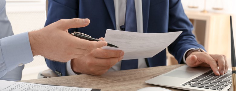 A suited man at a desk, handing over a legal document