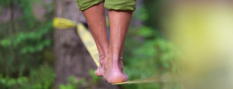 A close-up of bare feet slacklining between trees