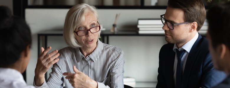 A grey-haired woman leads a business meeting in an office