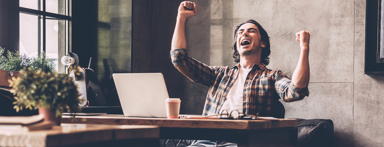 A man at a desk looking at a laptop and celebrating