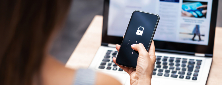 A woman on a laptop looking at her locked phone screen