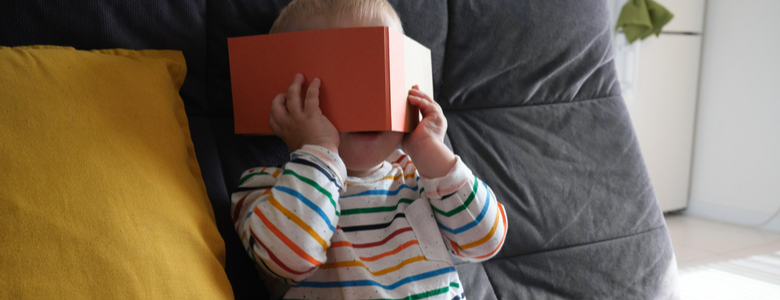 A toddler hiding behind an orange book
