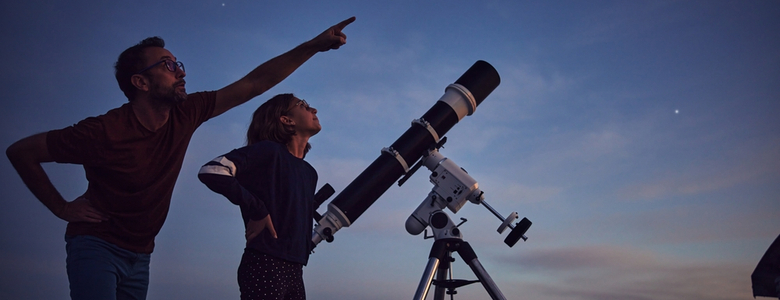 A man and woman look at the stars with a telescope.