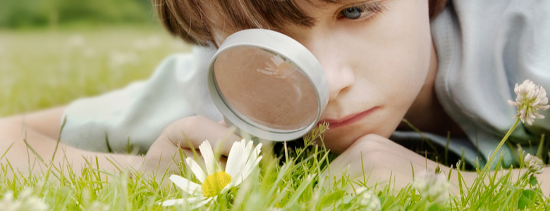 A young boy lying on the grass and looking through a magnifying glass