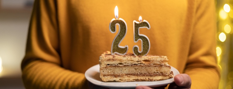 A person carrying a slice of cake with candles showing the number “25”