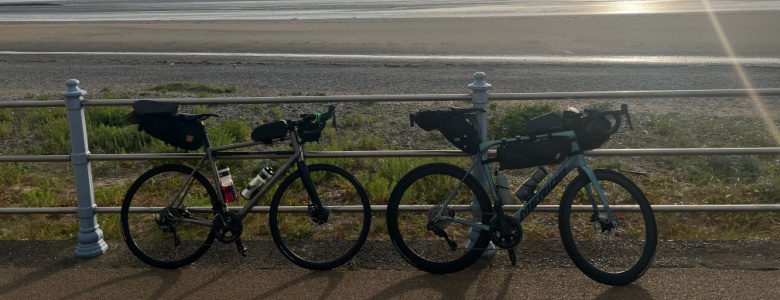 Two bikes leaning against railings by the sea at sunset